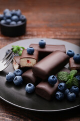 Delicious glazed curd snacks with fresh blueberries and mint served on wooden table, closeup
