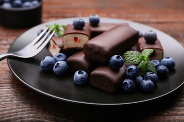 Delicious glazed curd snacks with fresh blueberries and mint served on wooden table, closeup