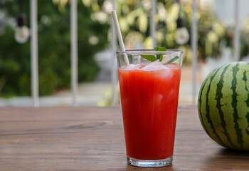 Glass of delicious watermelon drink with mint, ice cubes and fresh fruit on wooden table outdoors, space for text