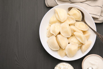 Delicious dumplings (varenyky) with cottage cheese served on black wooden table, flat lay. Space for text