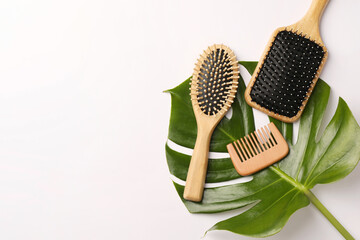 Wooden hairbrushes, comb and green leaf on white background, flat lay. Space for text