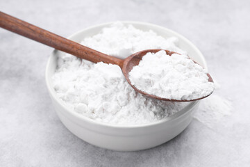 Spoon and bowl of starch on light gray table, closeup