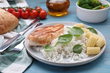 Grilled chicken breast and rice served with vegetables on light blue wooden table