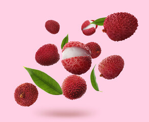 Fresh lychees with green leaves falling on pink background