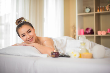 Obraz na płótnie Canvas Beautiful asian woman is lying comfortably on a white bed in the spa room and there have a glass of spa oil next to her while looking to the camera in spa room.