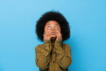 Fototapeta na wymiar Afro African boy doing funny ghost face in light blue isolated background studio shot