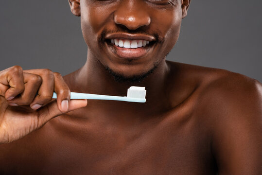 African American man smiling and holding toothbrush with toothpaste in light gray background studio shot