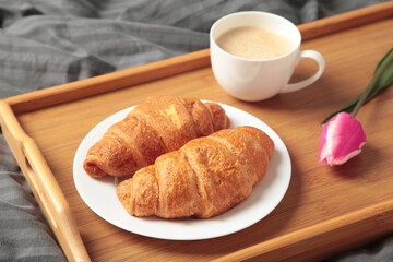 Breakfast in bed with coffee, croissants and tulip on tray