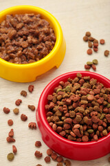 Wet and dry pet food in feeding bowls on light background. Vertical photo