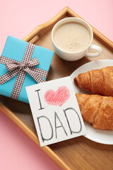 Father's day concept with gift, card and breakfast on tray. Breakfast for dad with croissant and coffee. Vertical photo