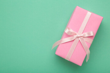 Pink gift box with ribbon and empty space for text on mint background. Holiday greeting background or invitation. Copyspace.