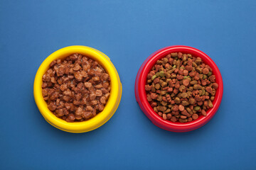 Wet and dry pet food in feeding bowls on blue background.