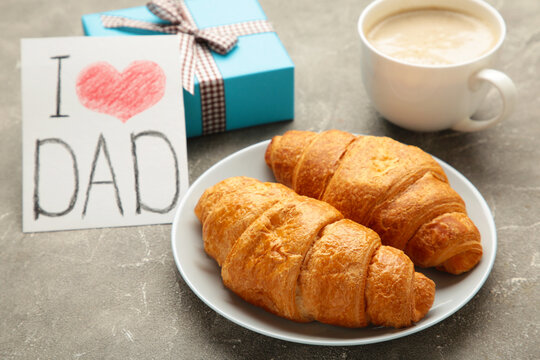 Father's day concept with gift, card and breakfast on grey. Breakfast for dad with croissant and coffee.