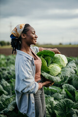 Portrait of a black smiling female farm worker holding a crate full of raw cabbage. © La Famiglia