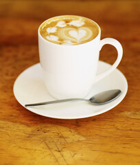 Latte art, coffee and drink on table in cafe, closeup of hot beverage and artistic heart design with milk foam. Cappuccino, espresso and creative pattern on caffeine liquid brew in a cup on a plate