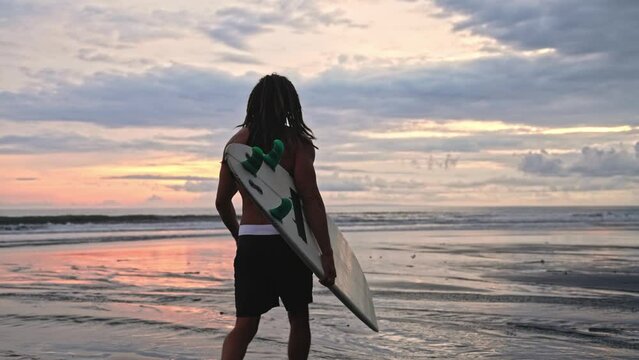 Man Surfer With Surf Board At Sea Nature And Ocean Water Waves On Background. Person At Coast Beach With Surfboard Going Away. Caucasian Guy At Seaside Bay Moves To Swimming or Surfing For Relaxation