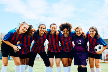 Multiracial women's soccer team on playing field looking at camera.