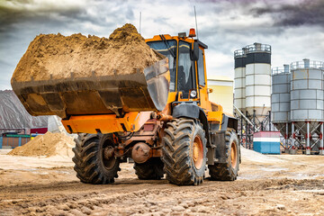 Powerful wheel loader or bulldozer working on a quarry or construction site. Loader with a full bucket of sand against the sky. Powerful modern equipment for earthworks.