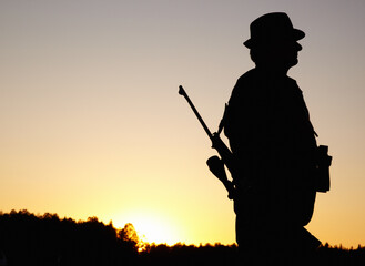 Hunting at sunset, man with rifle and mockup in nature to hunt game for sport hobby on safari adventure. African sky, silhouette and mock up space, hunter with gun in bush and evening setting sun.