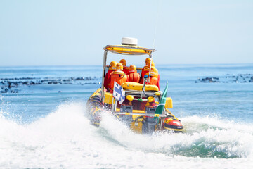 Rescue team on boat, safety in the ocean and transportation, emergency service with protection in the water. People on sea patrol with back view, search mission and security at the beach with help