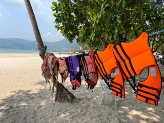 Tropical beach. Southeast Asia. Popular place for tourists. Water safety equipment. Multi-colored life jackets of different sizes are hung on a rope stretched between palm trees. Water, Rescue Service