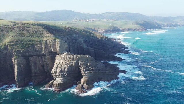 hazy coast aerial panoramic shot of waves crashing into the dreamy shore at Playa de Tagle, Spain. 