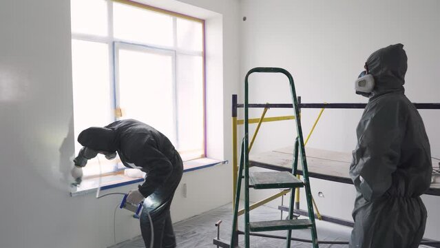 Teamwork, labor. Two house painter builders paint the walls in the room with spray paint
