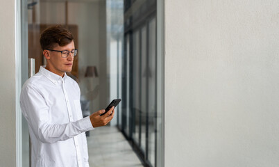 Businessman standing with smartphone in hand, hallway on backgro