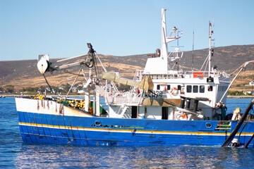 Naklejka premium Fishing boat, ocean and offshore with a commercial and fisherman transportation on water. Ship, harbor and nature with port outdoor by the sea with sailing and calm travel in summer in the sunshine