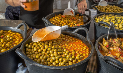 Wide selection of olives at a food stall a traditional market on a village street with the vendor preparing the order with ladle