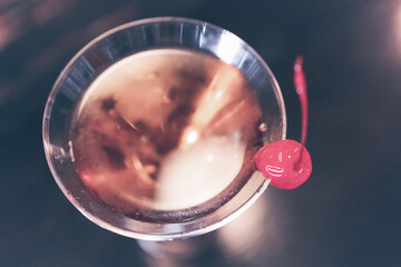 Warm, cozy bar interiors. Close up shot from above of a beautiful brown liqueur or drink in a martini glass, with a sweet red candied cherry on the edge of the glass. Adult relax.