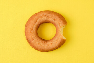 Half eaten plain donuts on yellow background.