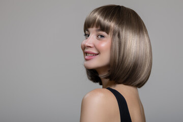 Fototapeta premium Portrait of a happy smiling brown-haired woman with shiny short hair. Gray background.