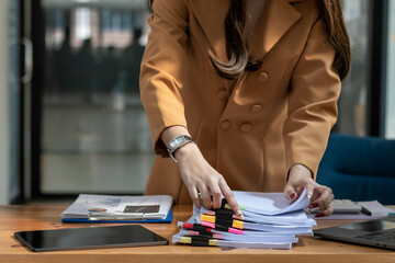 Businesswoman hands working on stacks of paper documents to search and review documents piled on...