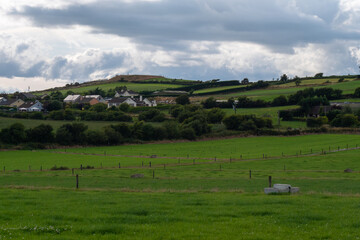 Fototapeta na wymiar A small village among fields and trees under a cloudy evening sky, County Cork. Rustic Irish landscape in summer, European village. Green grass field under cloudy sky