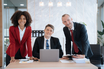 Business team smiling and confident standing in front of bright desk.