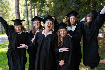 A group of graduates in robes congratulate each other on their graduation outdoors.