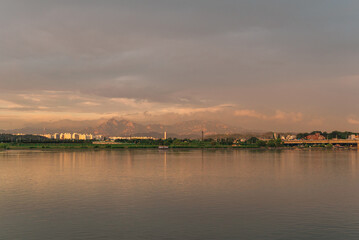 A mountain that looks like a golden color by the clouds behind the lake at sunset. And that...