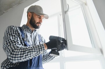 Naklejka na ściany i meble Worker installing plastic window indoors