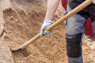man takes a shovel of sand from an embankment