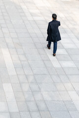 Back view of Asian businessman walking and talking on the phone outdoors.