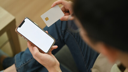 Young male consumer holding credit card and smartphone doing online banking transaction or shopping online