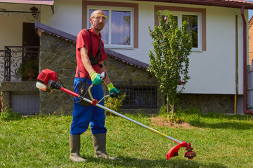 a man stands with a mower in the yard,a man mows the grass on the background of a house in the...