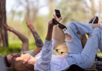 Group of young people having fun in park, sitting on the grass and using cellphone