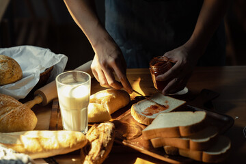 Man in apron preparing breakfast and spreading raspberry jam on slice of bread with table knife on cutting board