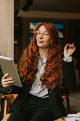 Smiley, happy, redhead business girl wearing eyeglasses working on her tablet