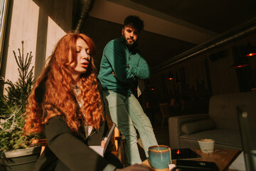 Low angle view of ginger woman working on her lap top while her male colleague is standing behind and following her