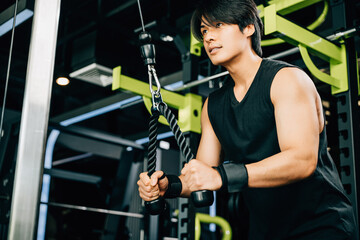 Asian man using a cable machine to do tricep pulldowns, focusing on building strength and maintaining a healthy lifestyle. Upper body strength exercise