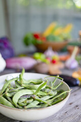 table on veranda of country village house with different vegetables, eco-friendly food from garden, autumn harvesting and plate with green bean pods