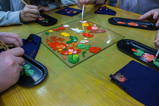 Zhostovo, Moscow region, Russia - October, 14, 2022: master class - painting a small black tray with bright flowers and leaves while holding brushes and paints at the table and copy space